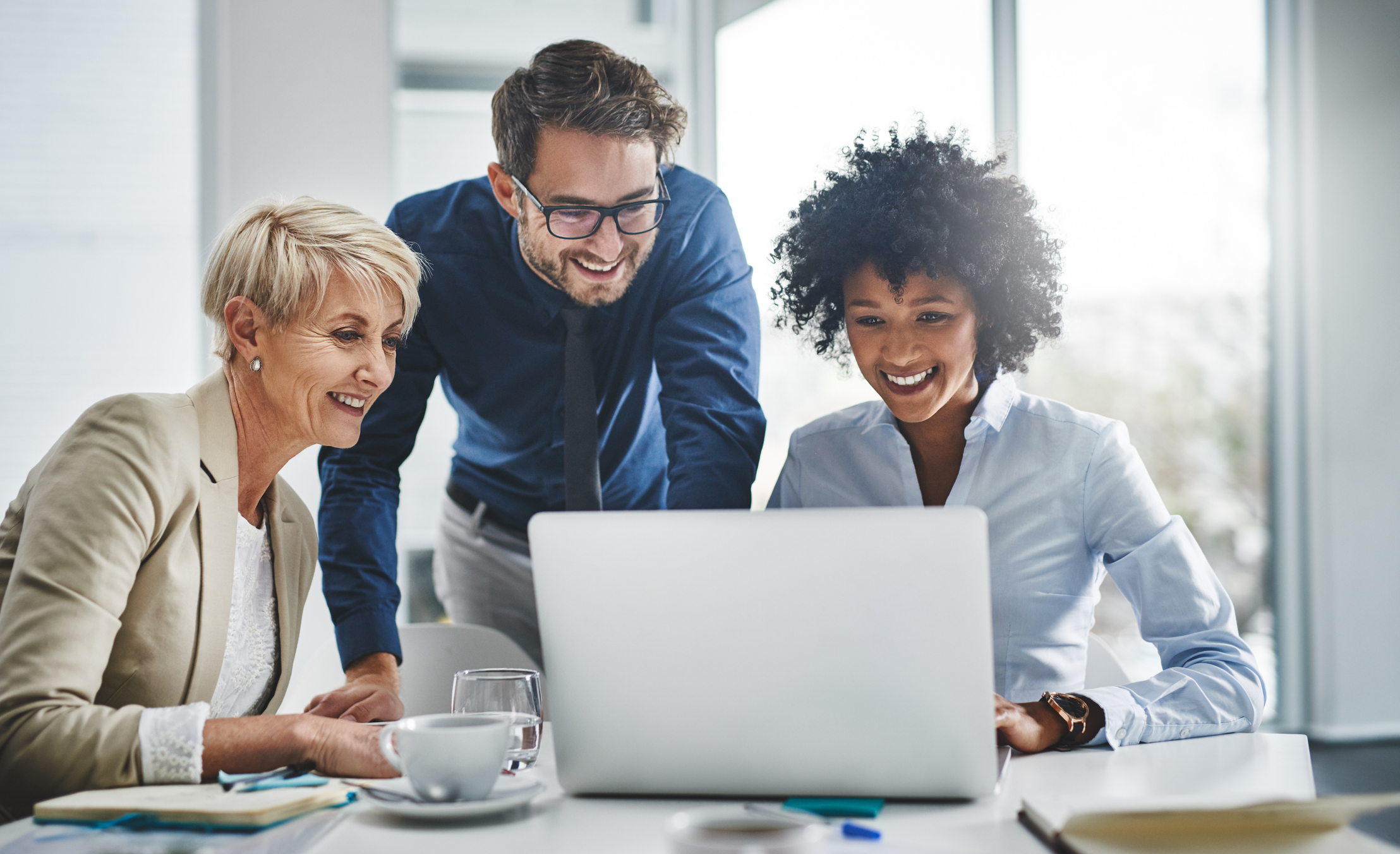 three people are looking at a laptop together and smiling