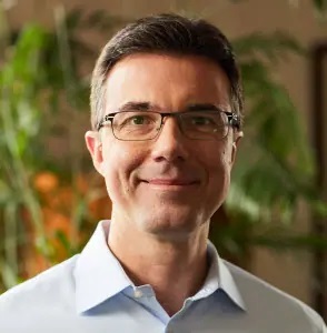 a man wearing glasses and a blue shirt is smiling for the camera .