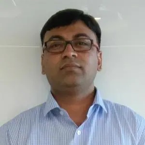 a man wearing glasses and a blue striped shirt is standing in front of a white wall