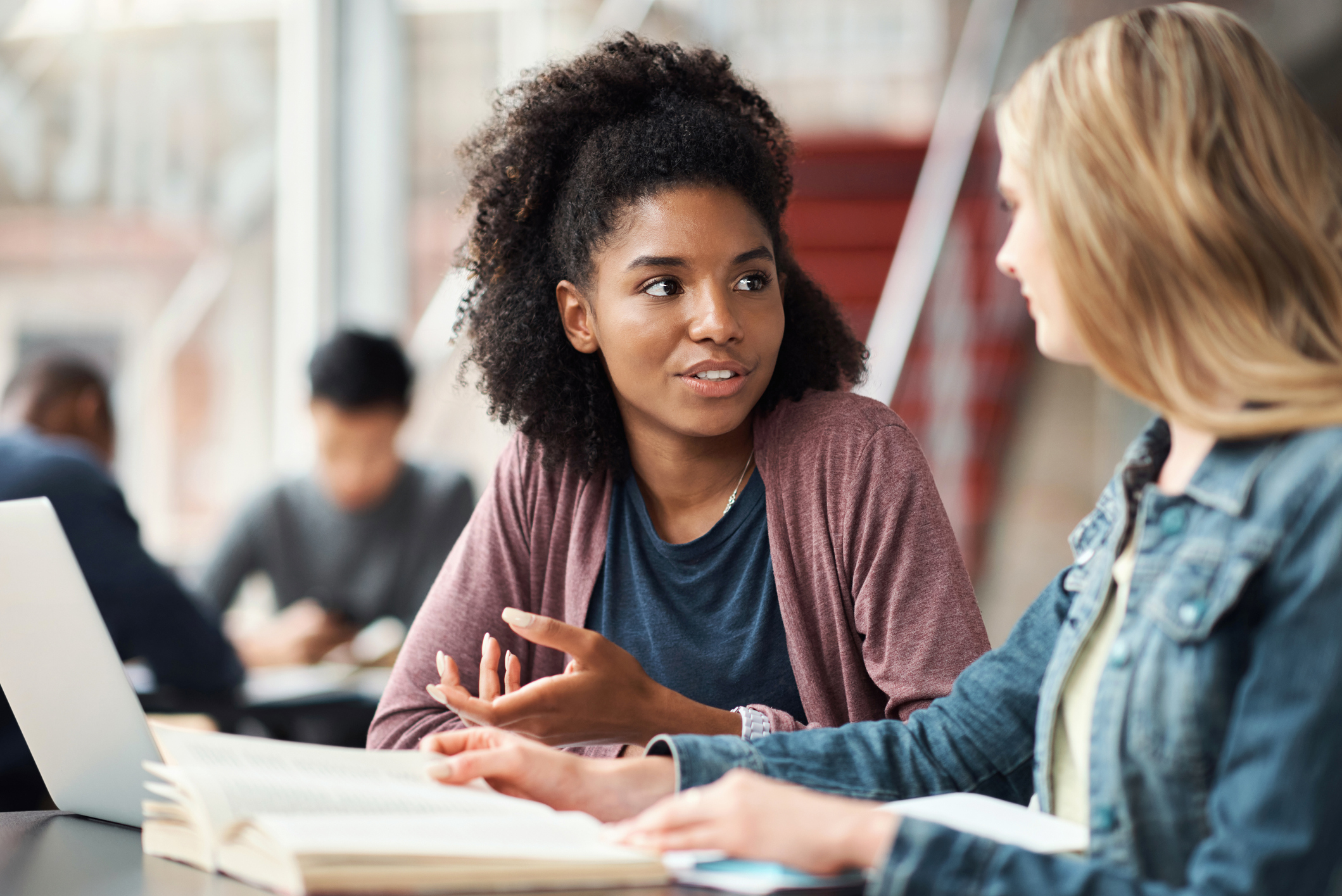 two women are sitting at a table with books and a laptop