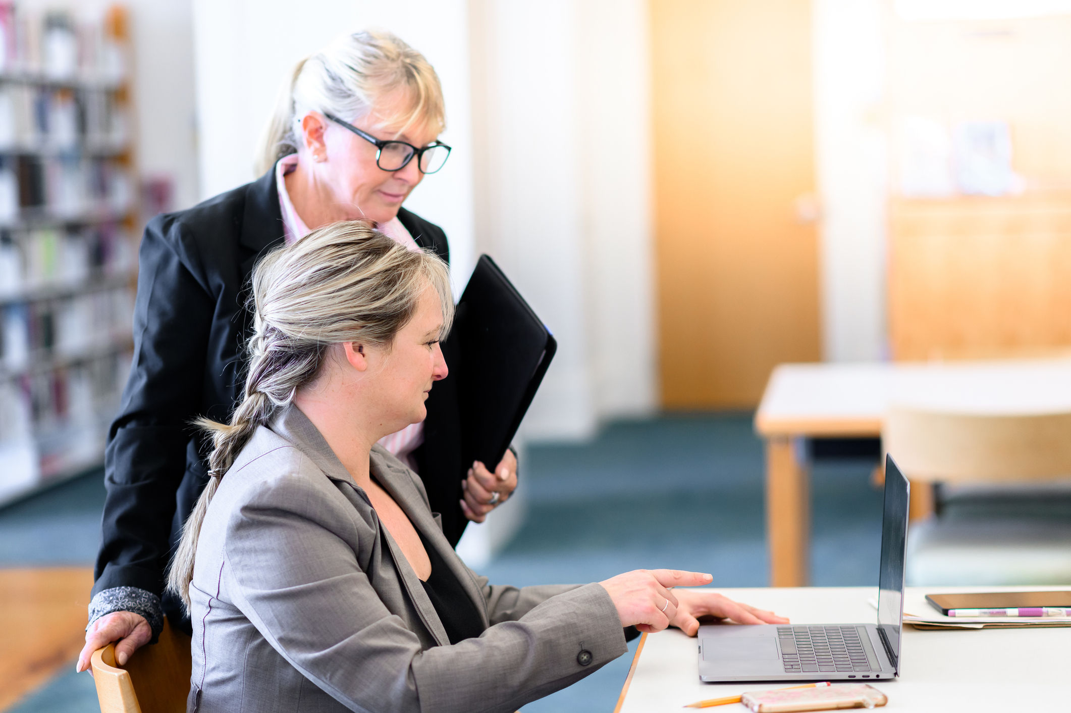 two women looking at a laptop in a library