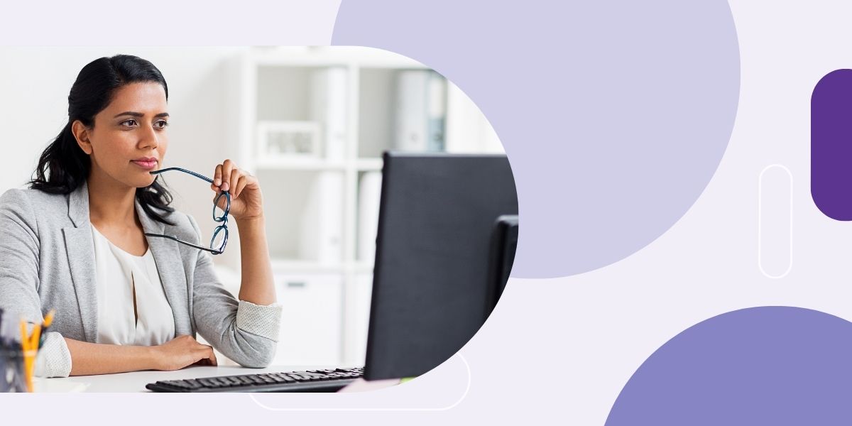 Photo of woman holding her eyeglasses looking at a computer monitor.