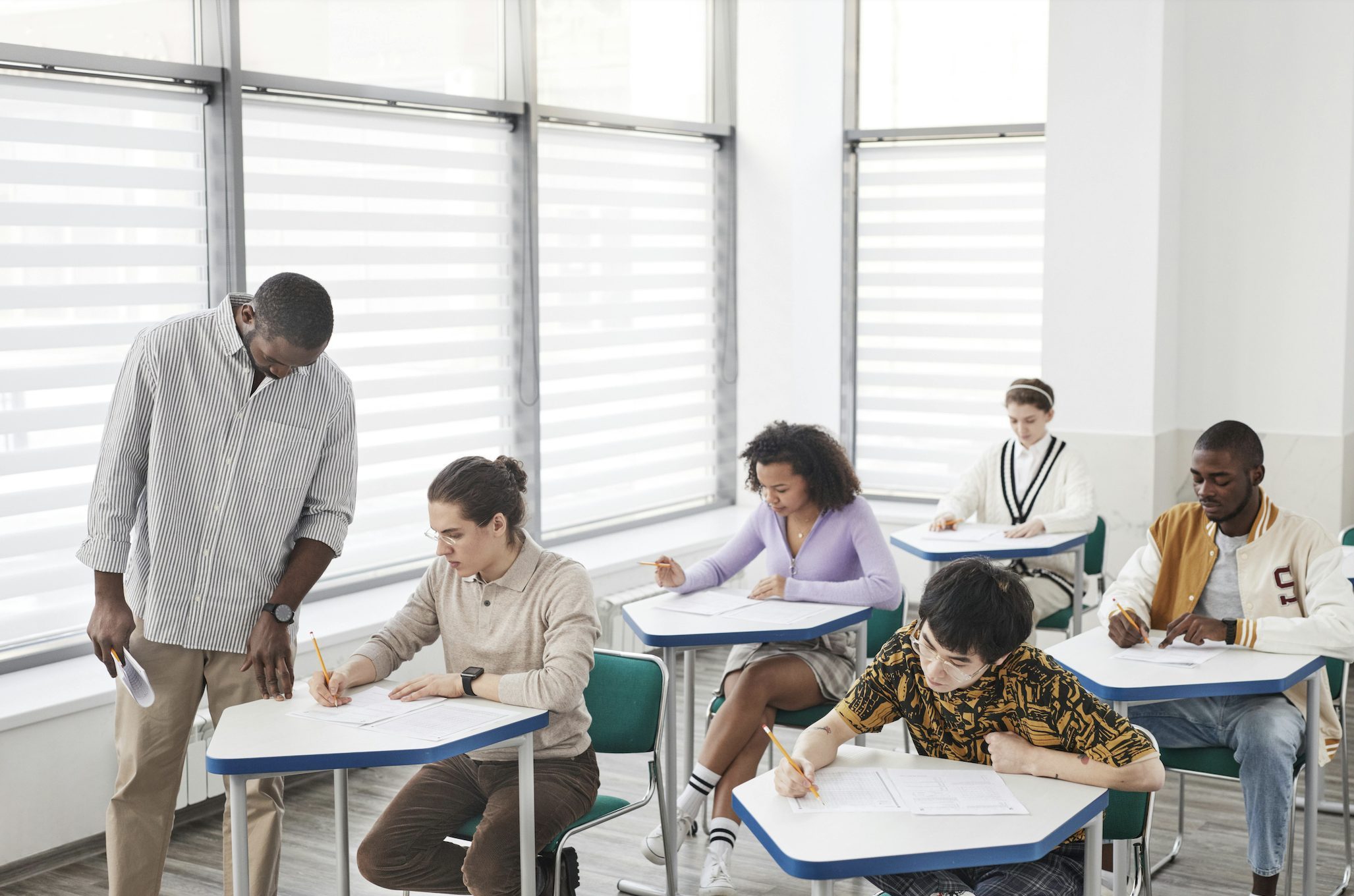 Students in a classroom a their desks with a teacher helping a student