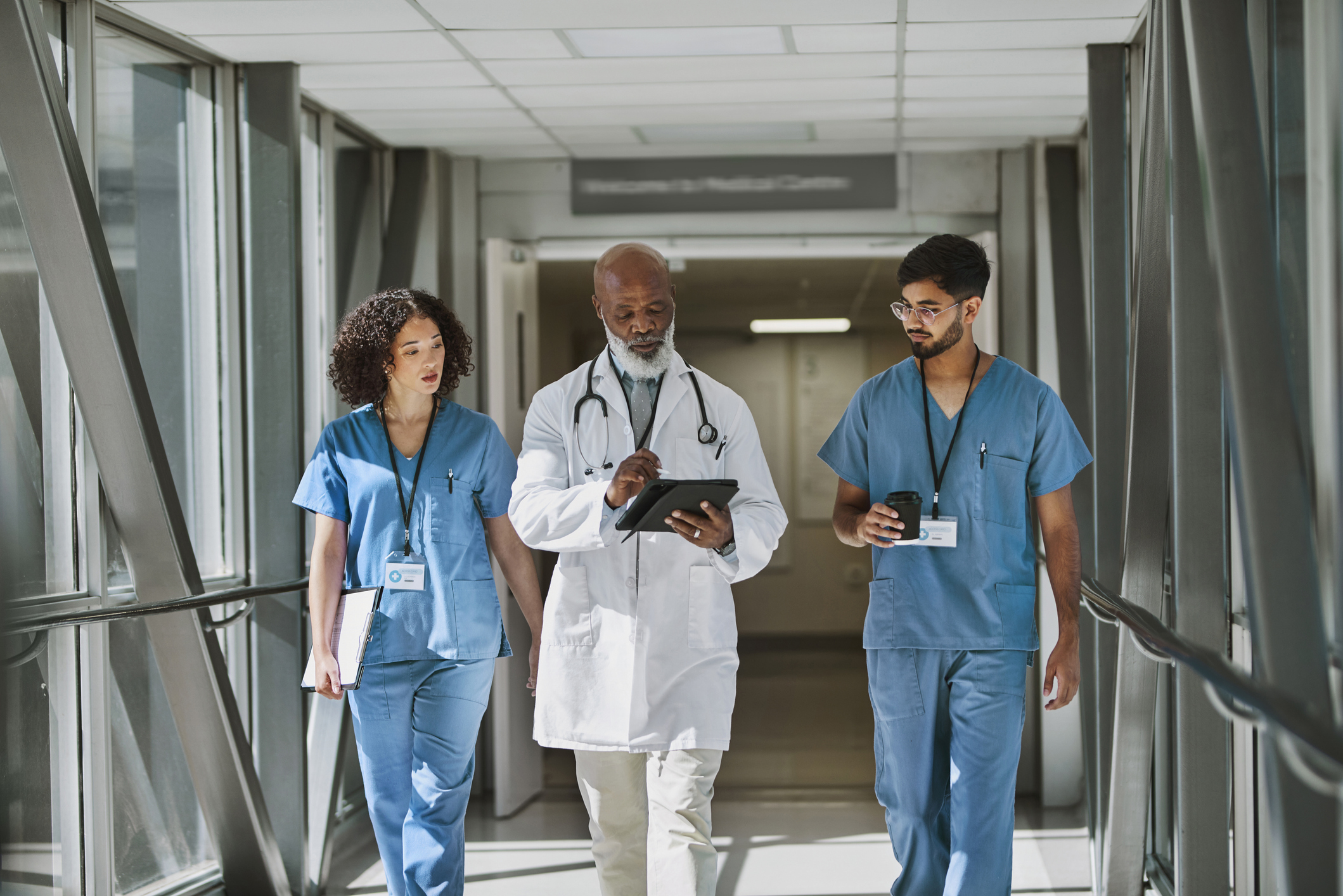 Senior doctor using digital tablet, walking with nurses in hospital corridor