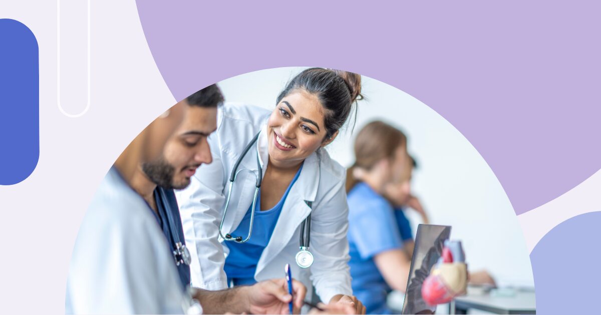 A group of medical students working on a laptop with a smiling medical school faculty member helping.